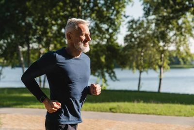 An older man running in a park with trees in the background
