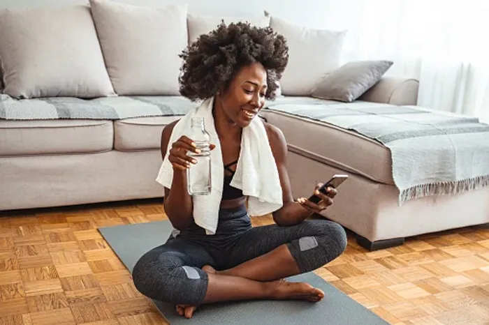 A woman sitting on a yoga mat looking at her phone - Top Hacks for the 24 Hour Fast