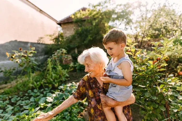 An older woman holding a young boy in her arms in a garden.