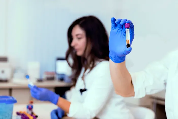 A woman in a lab coat and blue gloves holding a test tube.