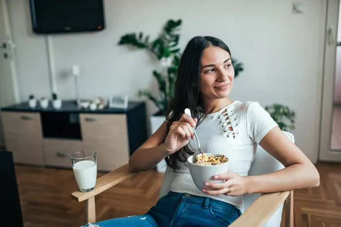 a woman sitting in a chair eating a bowl of cereal rich in folic acid