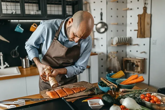 a man in an apron preparing salmon dish rich in omega 3 fatty acids