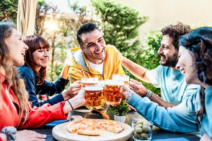 A group of people sitting around a table with pizza and beer - Does Beer Contain Probiotics? 